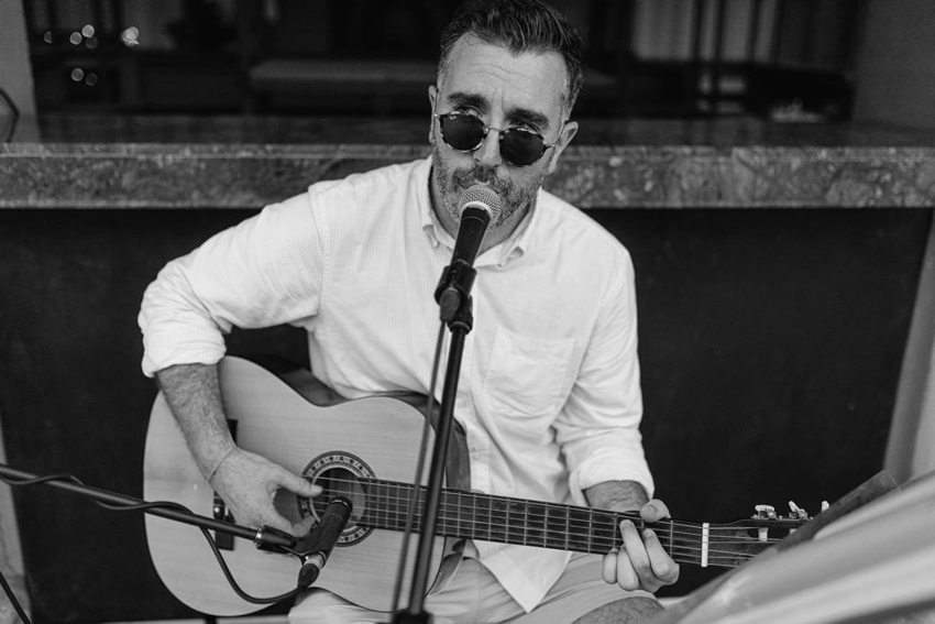 Black-and-white portrait of Matthew seated, singing and playing acoustic guitar