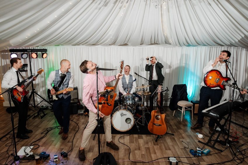 Matthew playing acoustic guitar with a full band and guests in a decorated marquee