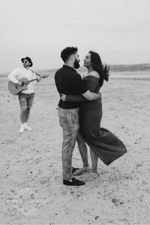 A couple embracing on the beach while Matthew plays guitar nearby