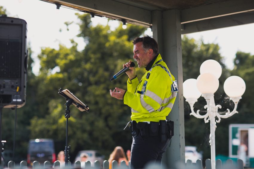 Matthew smiling and singing into a microphone in his police character costume