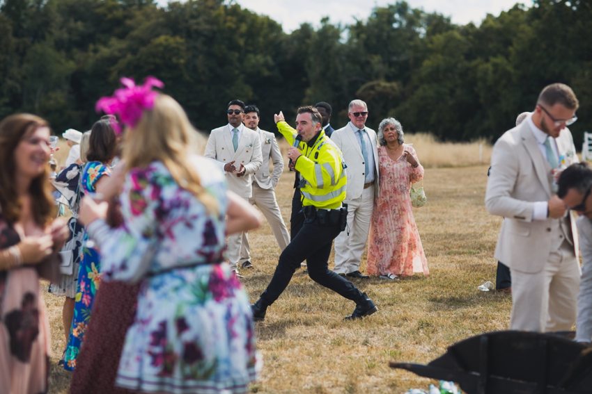 Matthew in police character striking an energetic pose while singing among wedding guests